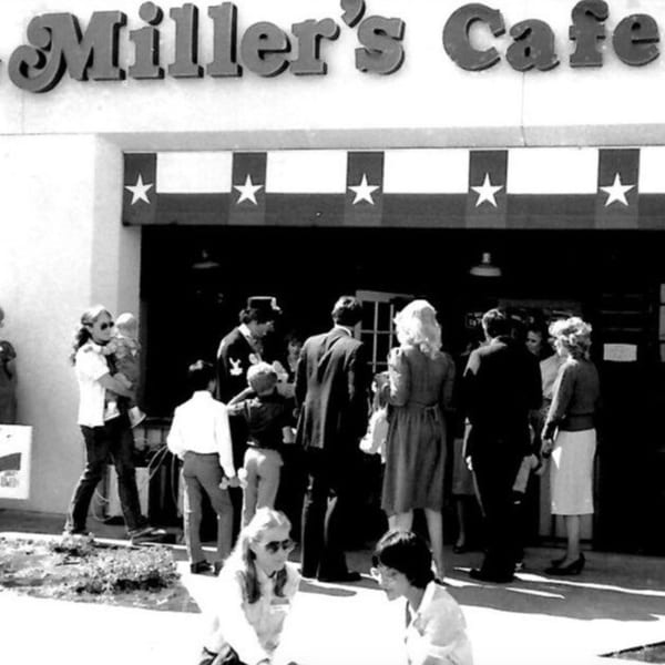 Black and white photo of a crowd gathered outside Miller's Cafe, with a star-spangled awning.