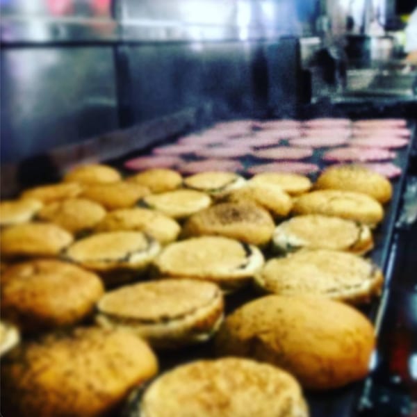 Many burger buns and patties cooking on a large flat-top grill at Miller's Cafe.