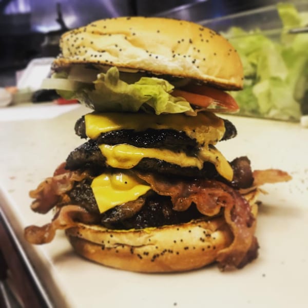 A towering Miller's Cafe triple cheeseburger with bacon, lettuce, tomato, and onion on a poppy seed bun.