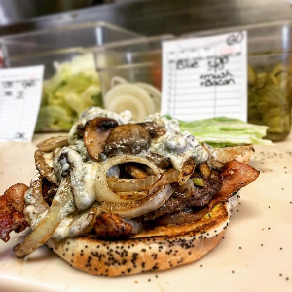 A Miller's Cafe burger with bacon, grilled onions, mushrooms, and melted cheese on a poppy seed bun.