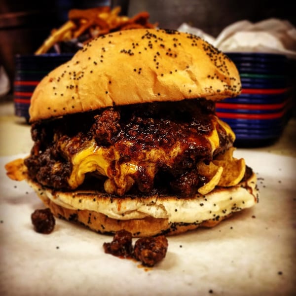 A messy, chili-covered Miller's Cafe burger with melted cheese and a poppy seed bun.