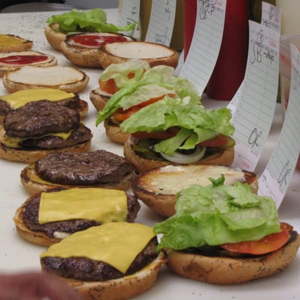 Multiple Miller's Cafe burgers being assembled with patties, cheese, lettuce, tomato, and onions.
