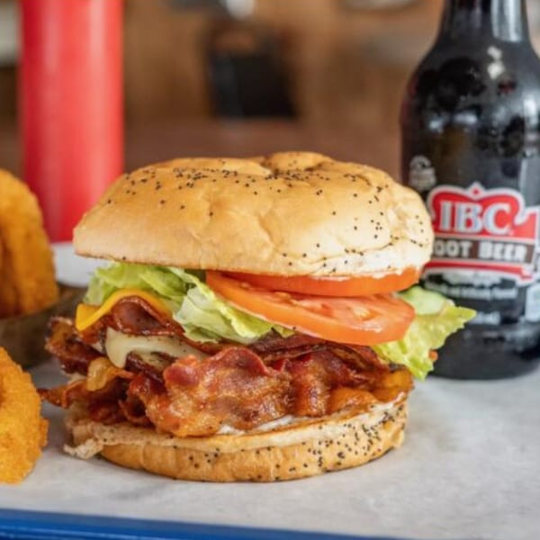 A bacon cheeseburger with lettuce and tomato, onion rings, and a bottle of IBC Root Beer.