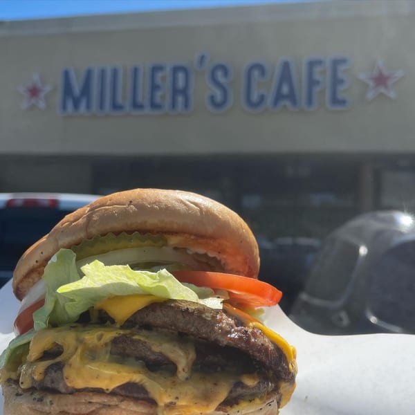 A double cheeseburger with lettuce, tomato, and pickles in front of Miller's Cafe sign.